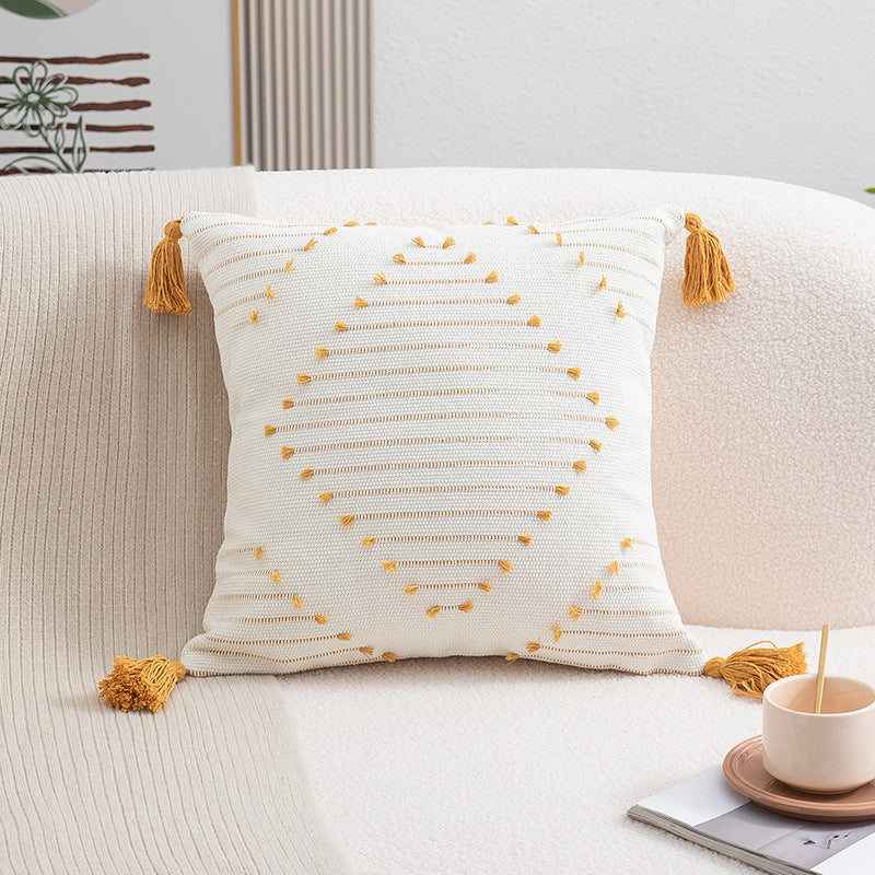 Decorative pillow with tassels on a sofa with a cup and saucer in the background